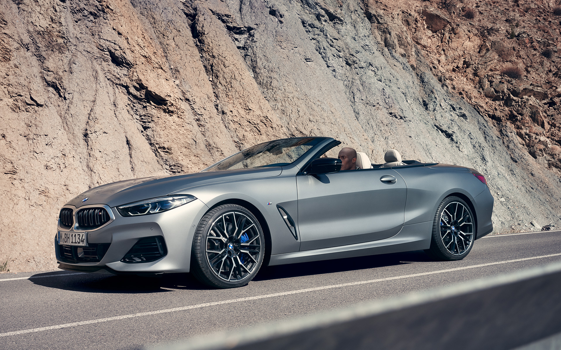 La nouvelle BMW M850i xDrive Cabrio G14 LCI restylage 2022 BMW Individual Frozen Pure Grey metallic, vue de trois quarts avant en mouvement devant des roches